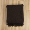 Dark brown woven blanket with fringes on a wooden floor