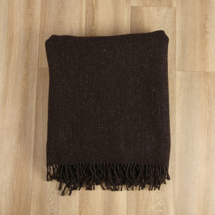 Dark brown woven blanket with fringes on a wooden floor