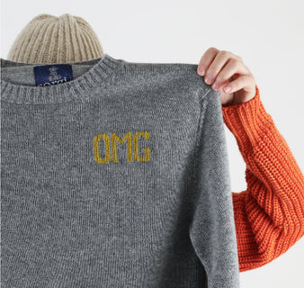 Person holding a gray sweater with 'OMG' embroidery on a white background