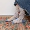 A pair of socks featuring a pattern of corgi dogs in various poses, worn on the feet of a person seated on a patterned rug.