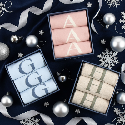 Three boxes of folded socks with lettering on a festive background with ribbons and ornaments.