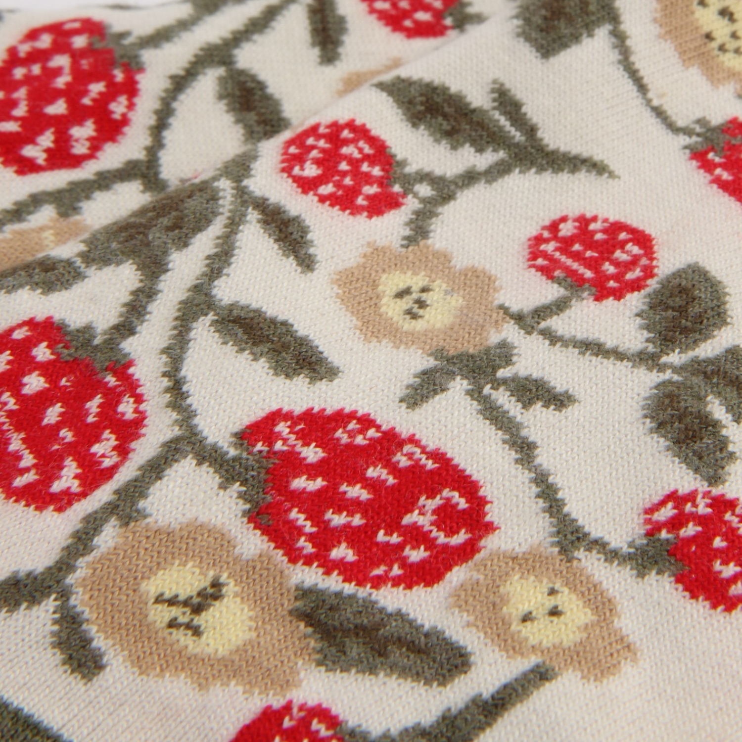 Close-up of a textured fabric with red floral patterns and strawberrys on a beige background