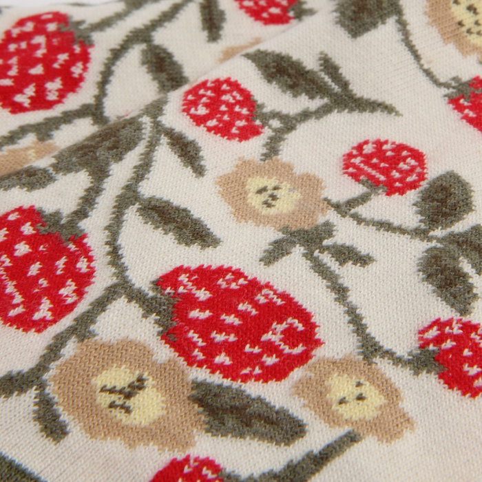 Close-up of a textured fabric with red floral patterns and strawberrys on a beige background