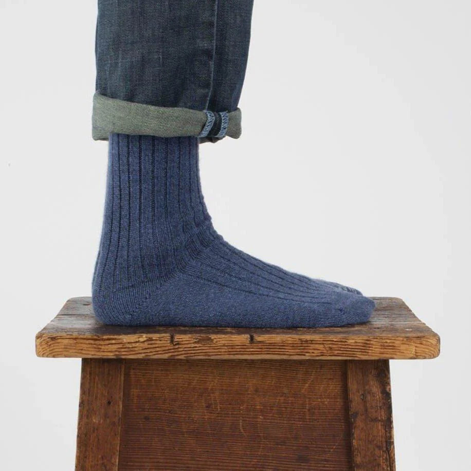 person wearing denim blue wool & cotton socks on a wooden stool