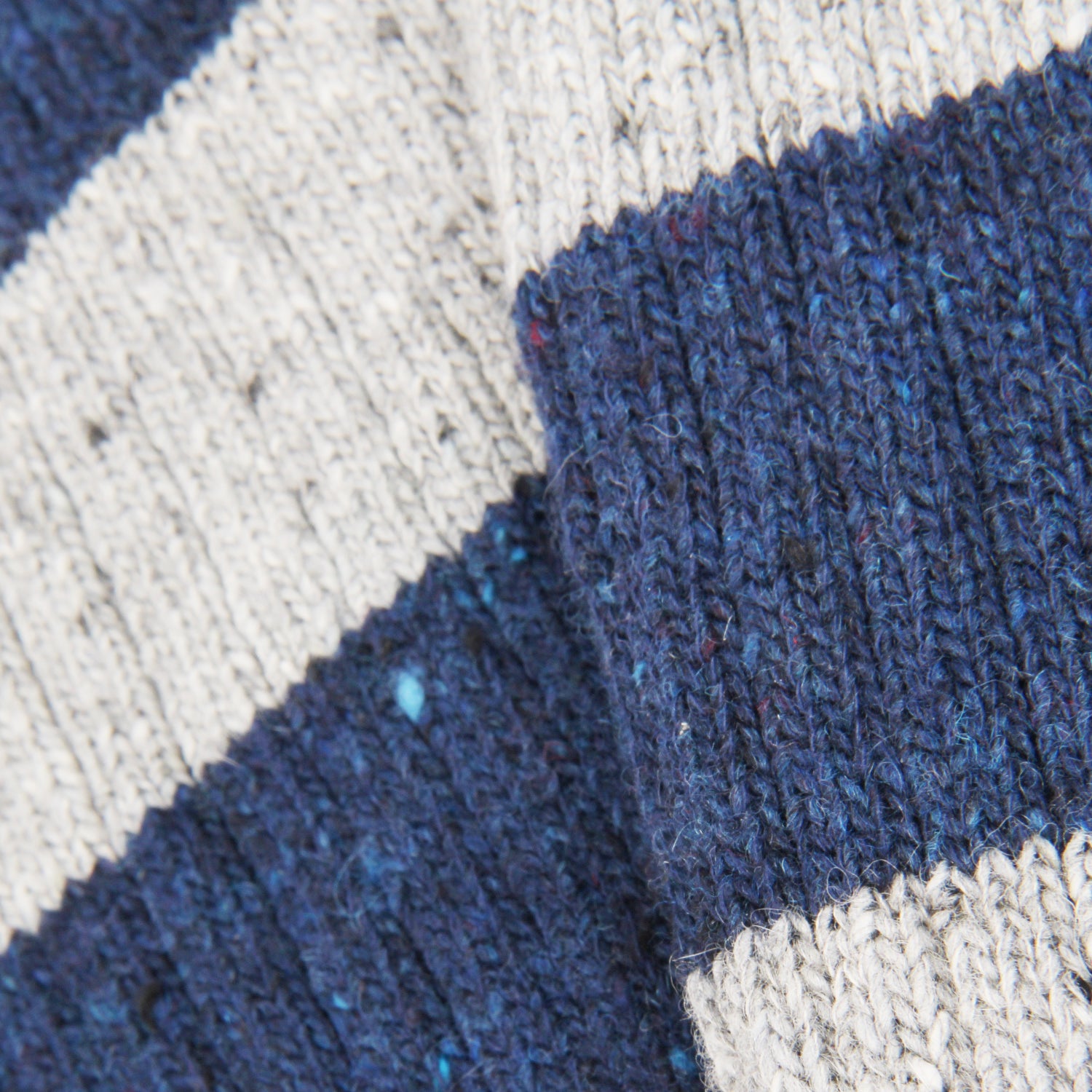 Close-up of a chunky knit fabric with alternating thick stripes in dark navy blue and warm off-white/cream.