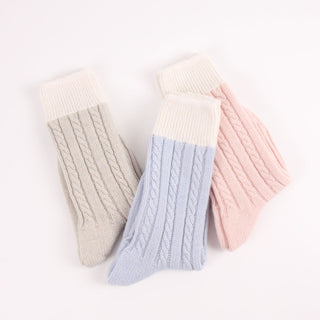 Three pairs of knitted socks in beige, light blue, and pink on a white background

