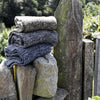Stack of folded scarves on a stone surface with a wooden post and greenery in the background