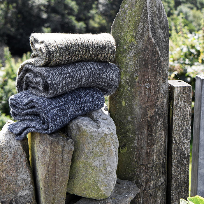 Stack of folded scarves on a stone surface with a wooden post and greenery in the background