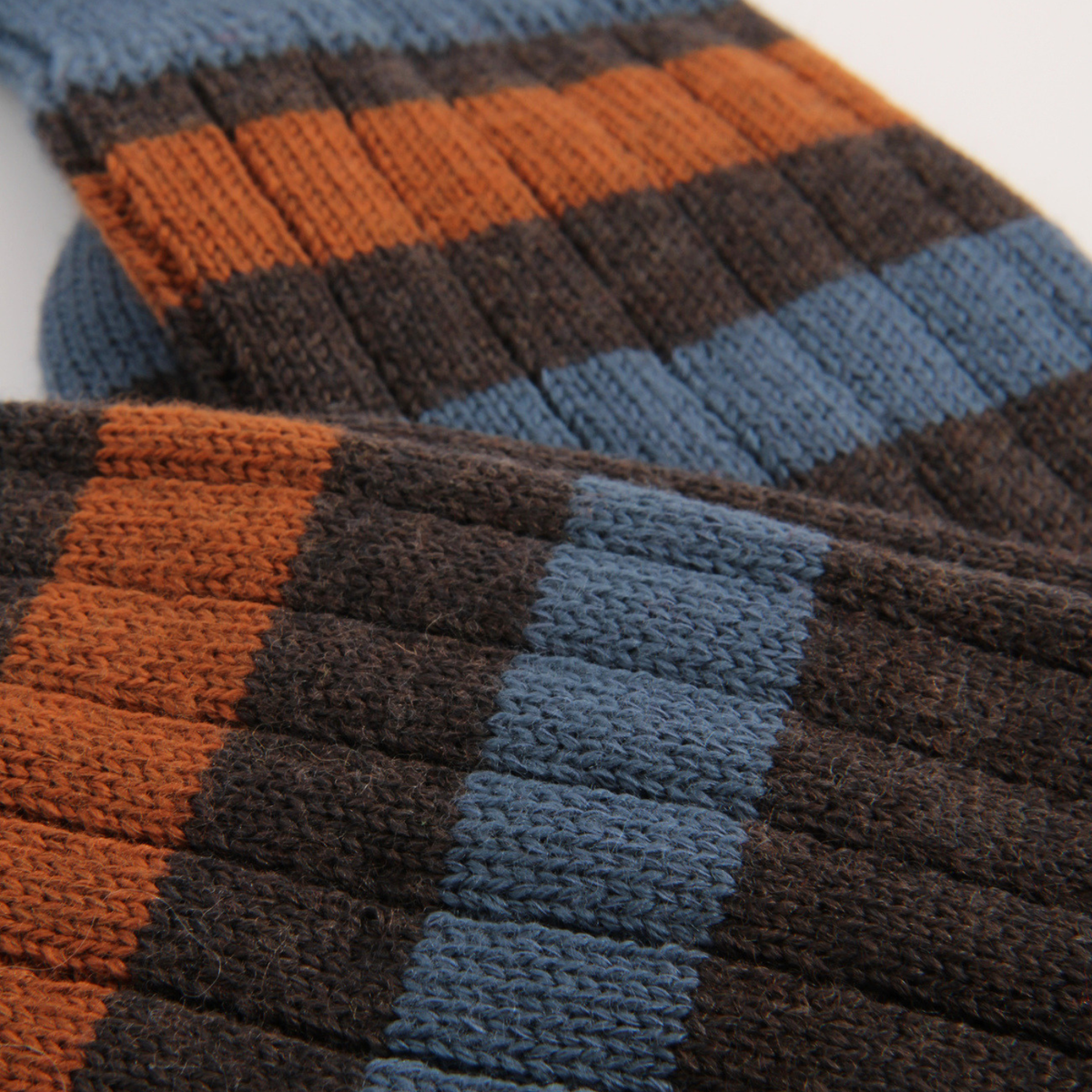 Close-up of a ribbed knit textile with wide horizontal stripes in rust orange, dark brown, and muted blue on a white background.