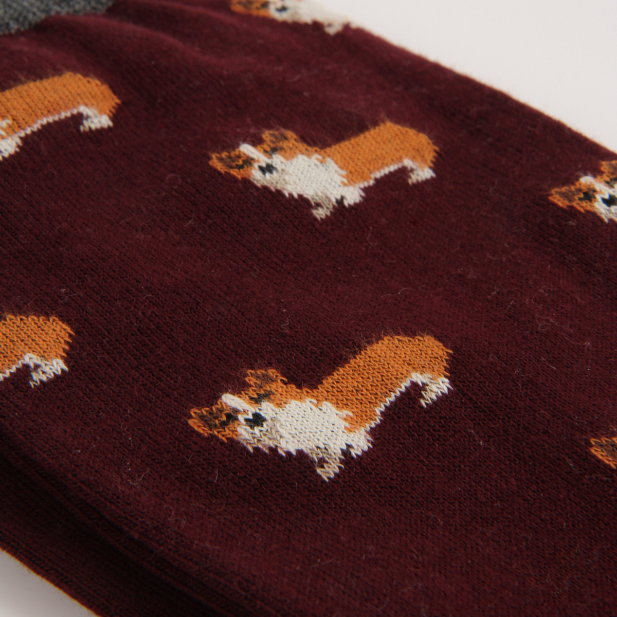 A close-up of a pair of dark burgundy socks featuring a repeating pattern of small brown and white dog illustrations.