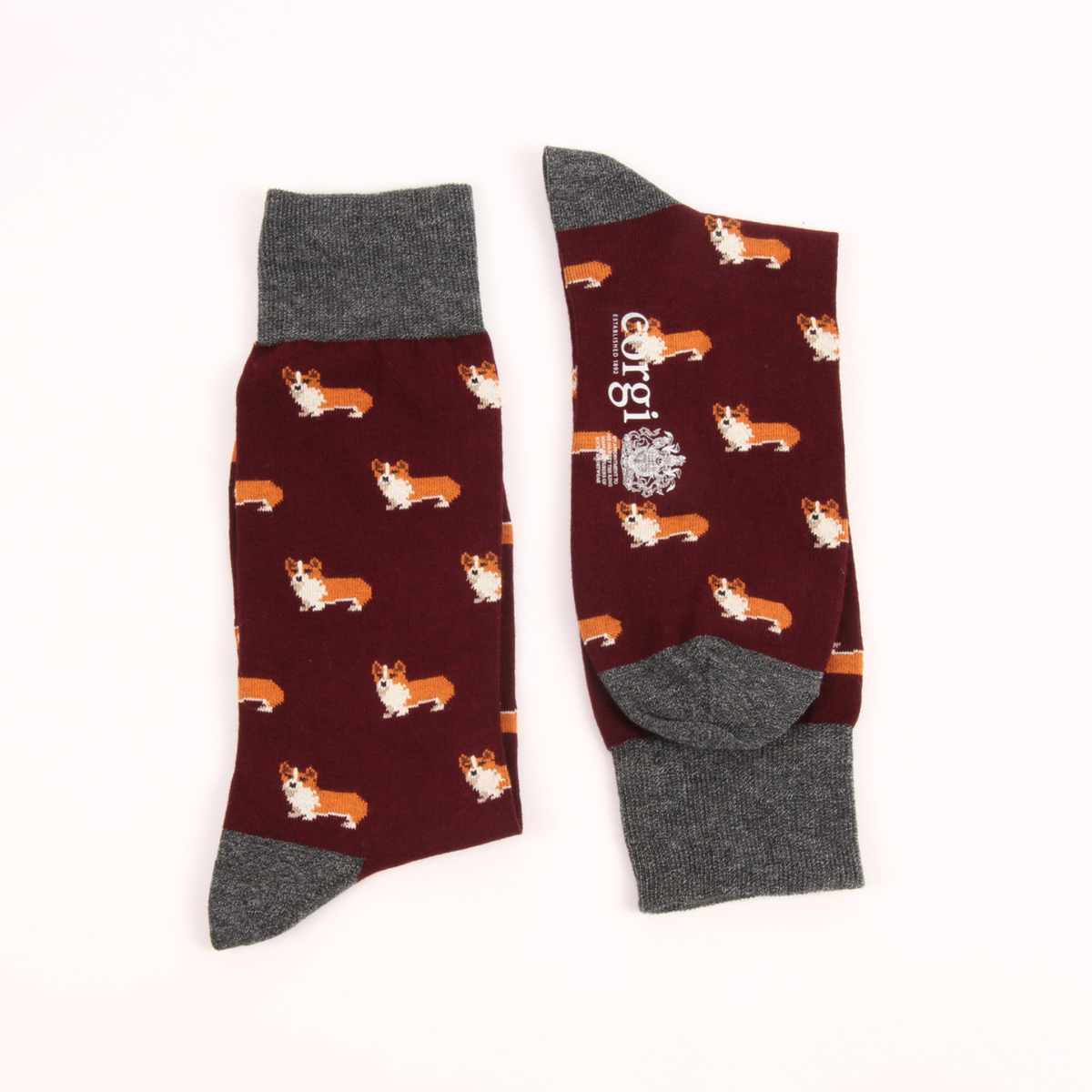 A pair of crew socks with a dark maroon background patterned with small Corgi dogs, featuring dark gray cuffs, heels, and toes. One sock is shown flat with the pattern, and the other is laid on its side showing the brand name 'Corgi' printed vertically on the side.