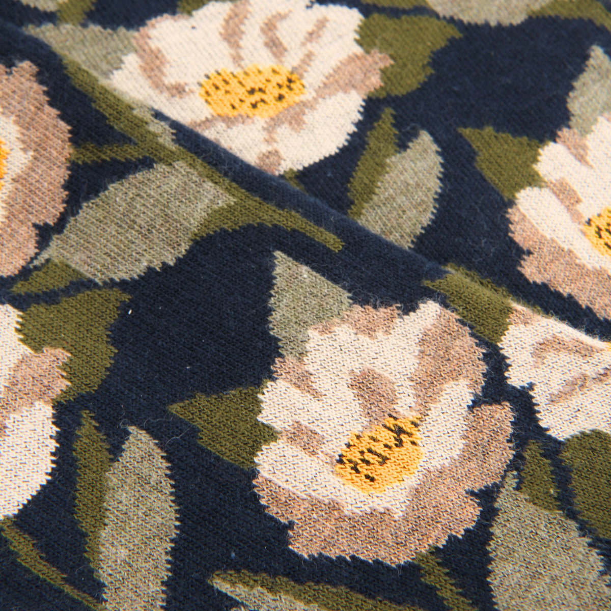 Close-up of a woven floral textile pattern with cream and blush flowers, olive green leaves, and a dark navy background.