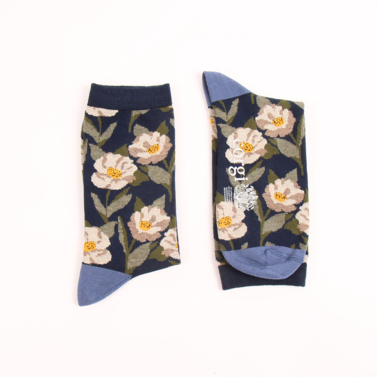 A pair of crew socks with a navy blue background, featuring a floral pattern of cream and pink flowers with yellow centers, olive green leaves, and light blue heels and toes, displayed flat on a white background.