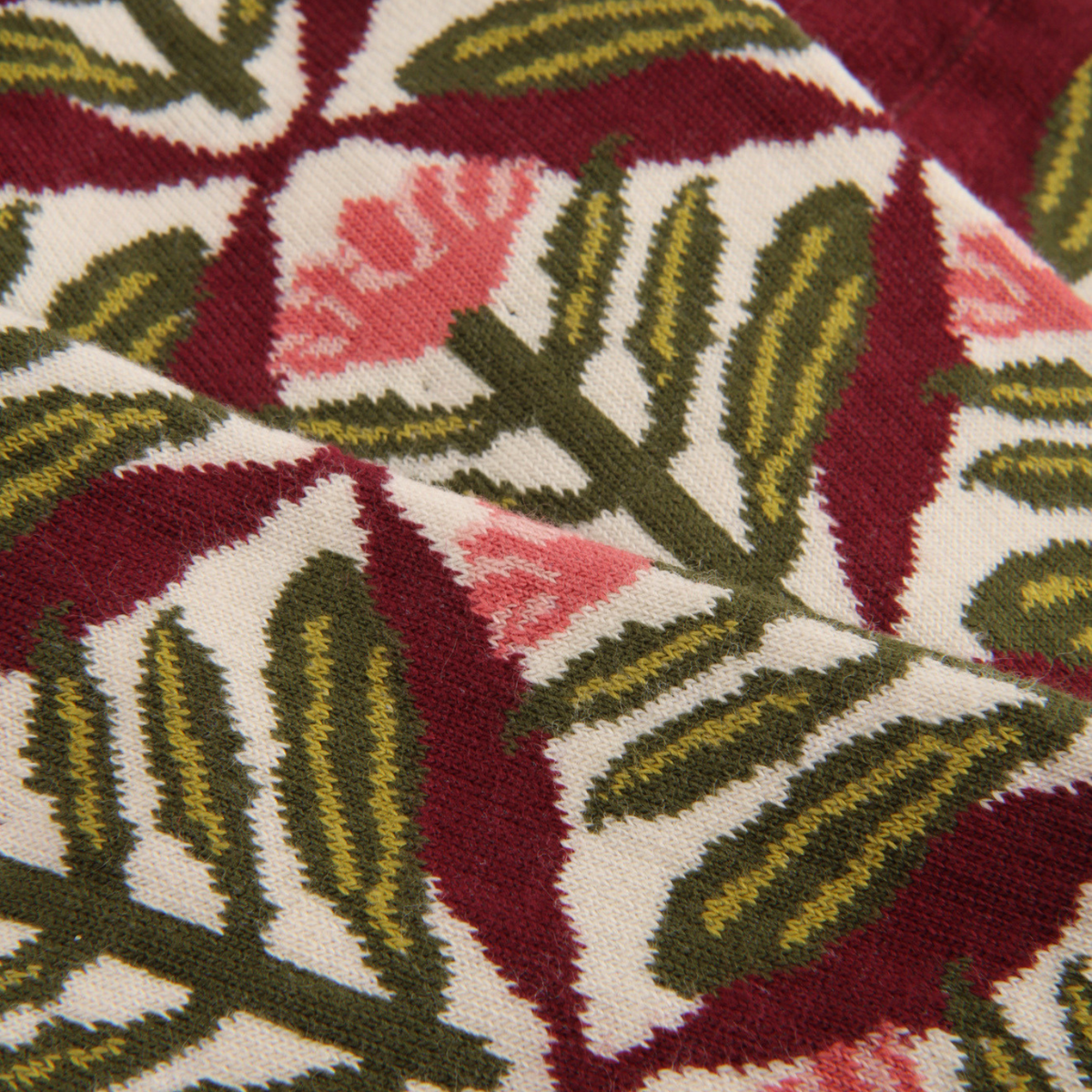 Close-up of a knitted fabric with a repeating geometric and floral pattern in burgundy, cream, olive green, and pink.