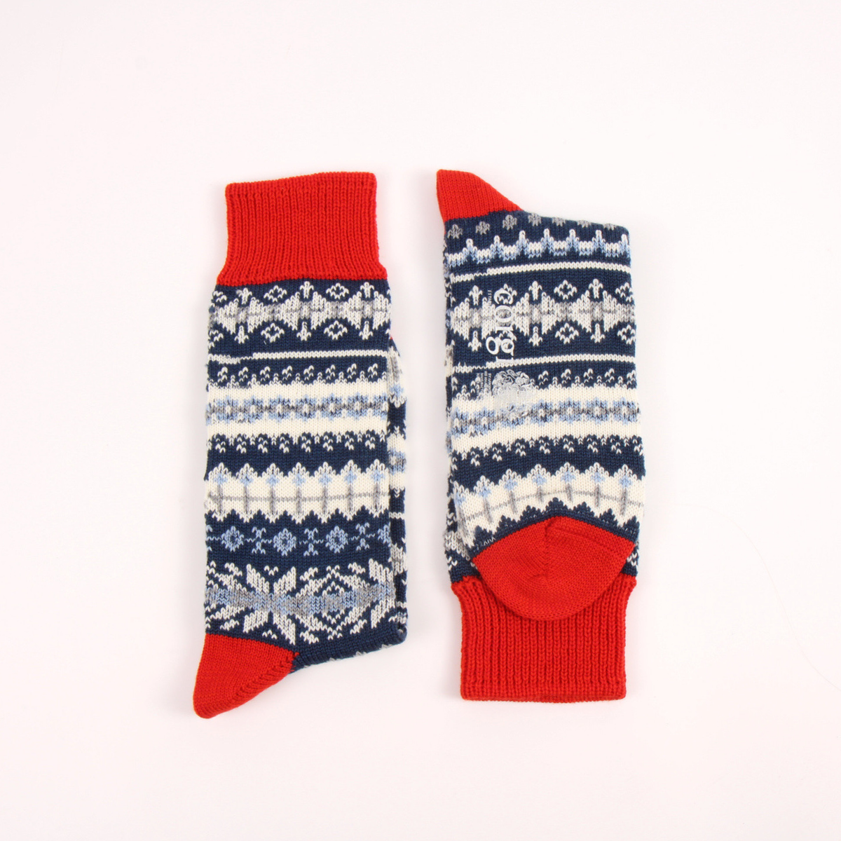 A pair of knit socks laid flat on a white background, featuring a navy blue and white Fair Isle pattern with solid red cuffs, heels, and toes.