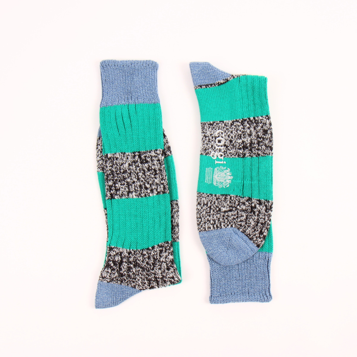 A pair of crew socks laid flat on a white background, featuring horizontal stripes of solid teal green, black and white marled knit.