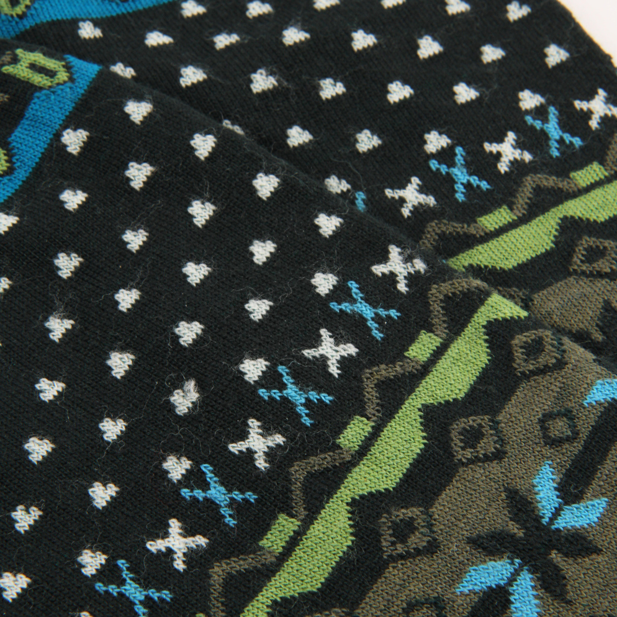 Close-up of a knit sock or fabric with a black base, white snowflake-like dots, light blue snowflake motifs, and olive green geometric border details.