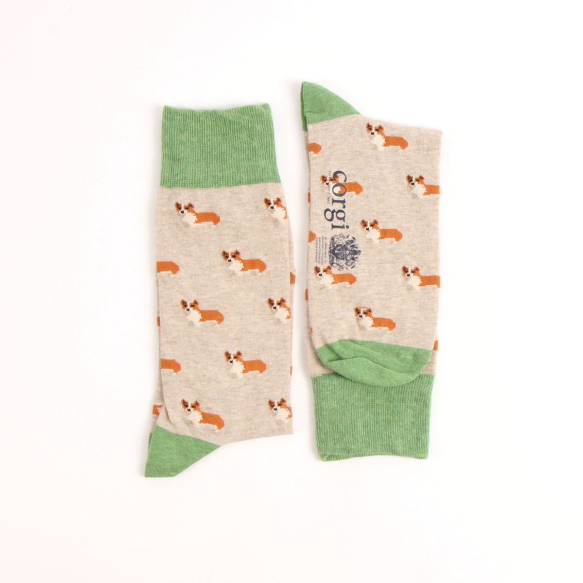 A pair of crew socks laid flat on a white background. The socks have a light beige heather base printed with small corgi dog illustrations in orange, white, and brown, with solid sage green cuffs, heels, and toes.