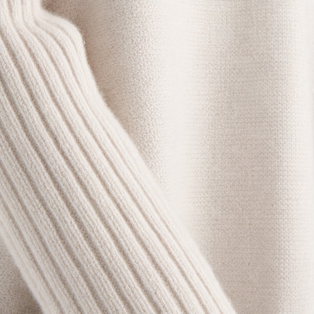 Close-up of a cream-colored knit fabric with a ribbed cuff and smooth textured body.