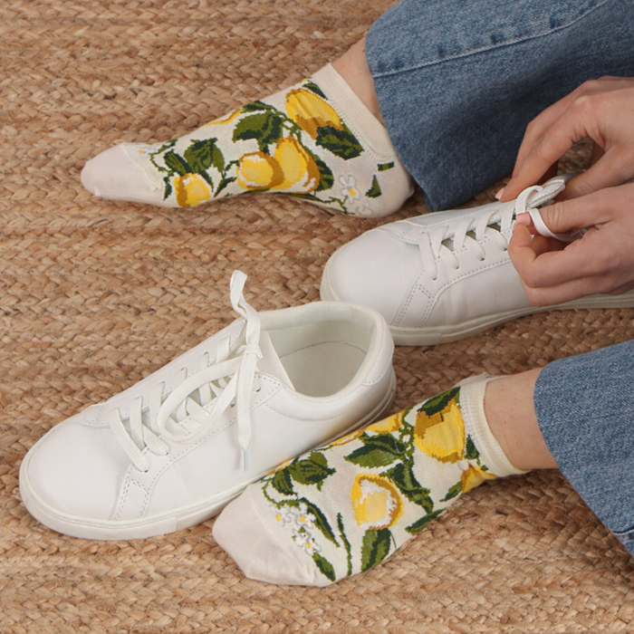 Person wearing white sneakers and lemon-patterned socks on a carpeted floor.