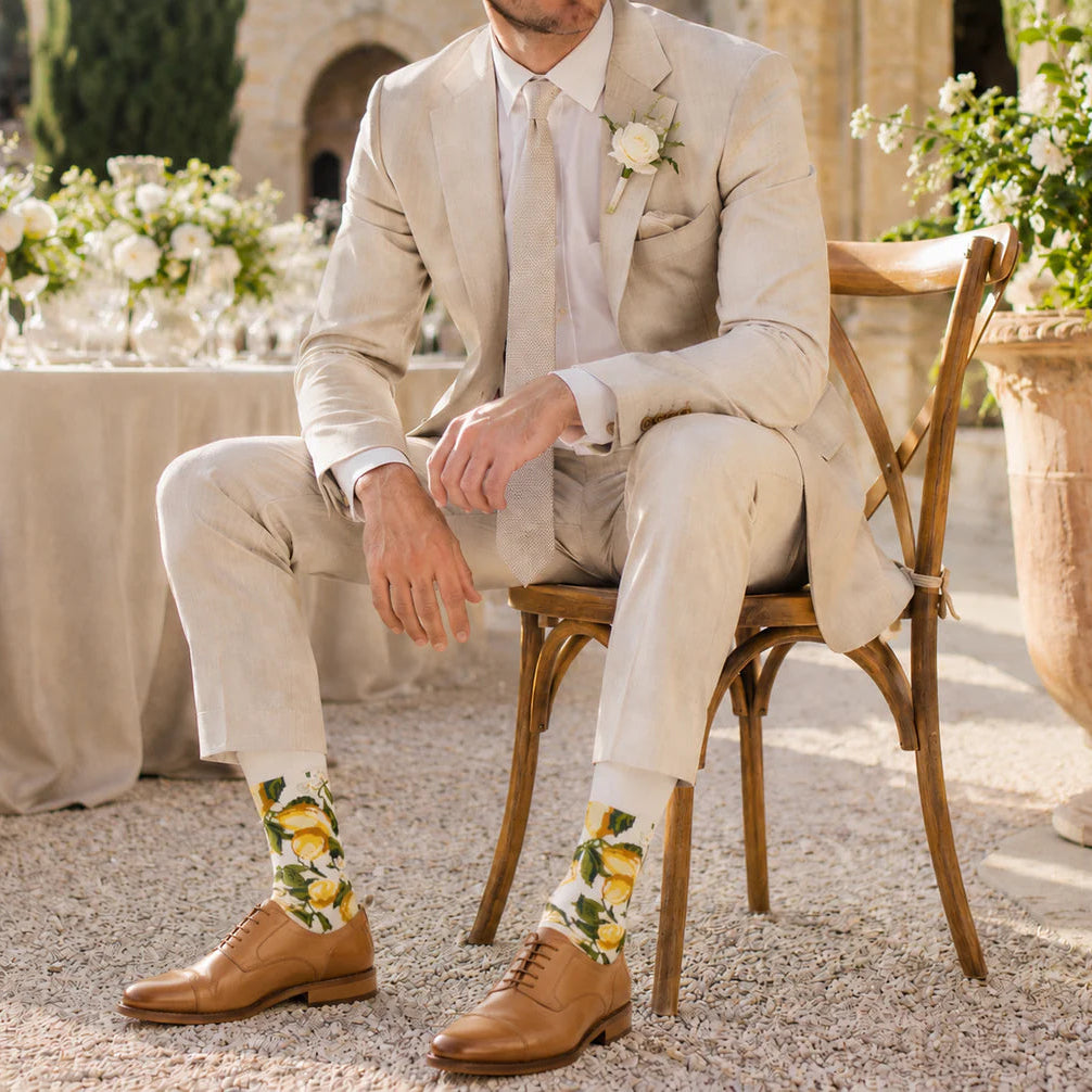 Man in a light suit sitting outdoors with floral decorations and a table in the background
