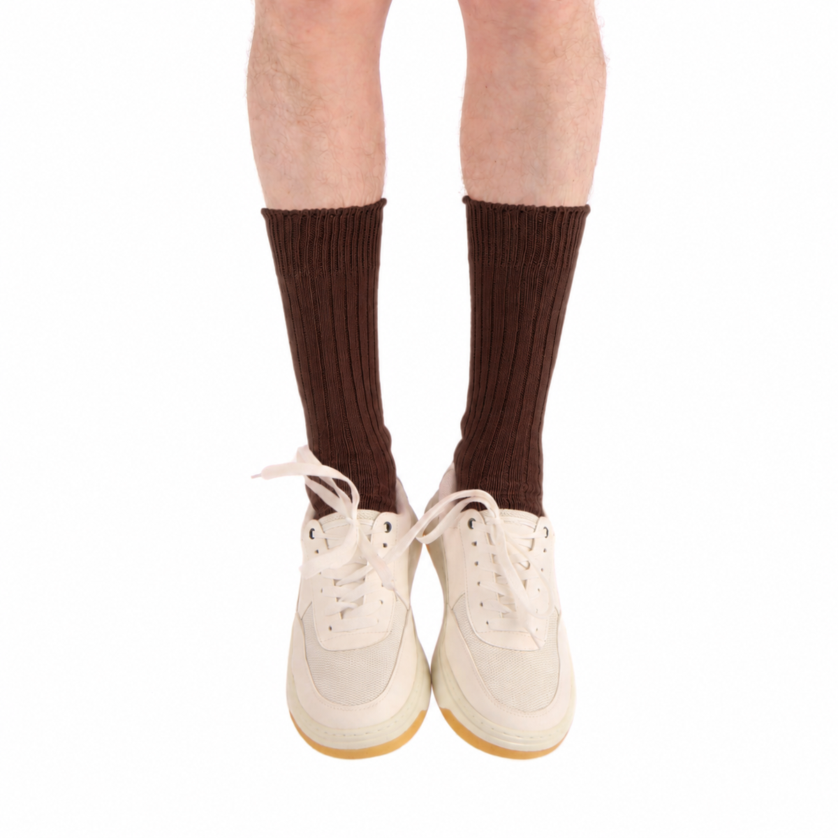 A person's legs wearing dark brown ribbed crew socks and off-white low-top sneakers with gum soles, shown against a plain white background.