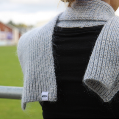Person wearing a grey knitted scarf over a black top with a blurred outdoor background