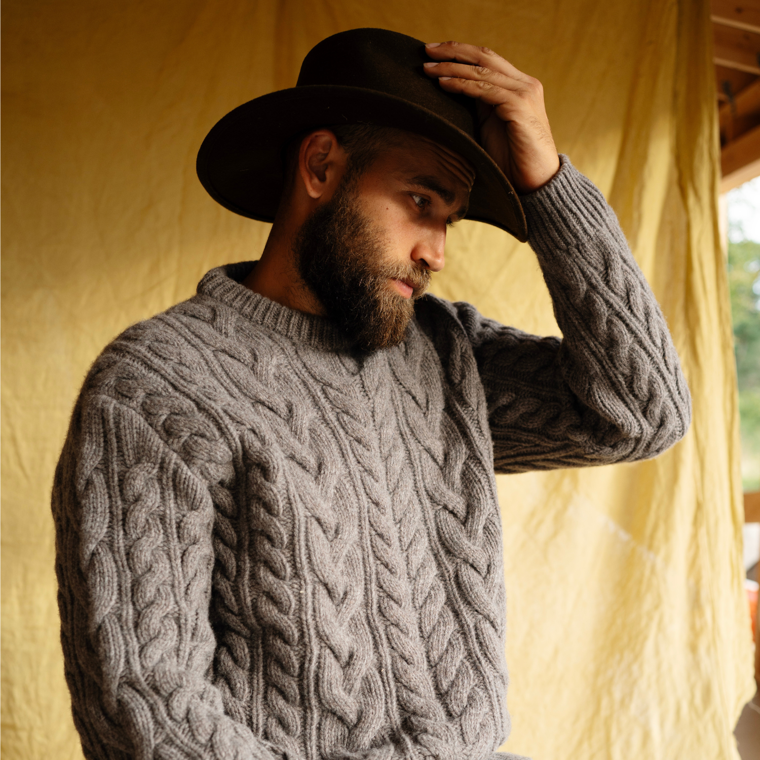 Man wearing a brown cable knit sweater and dark hat indoors.