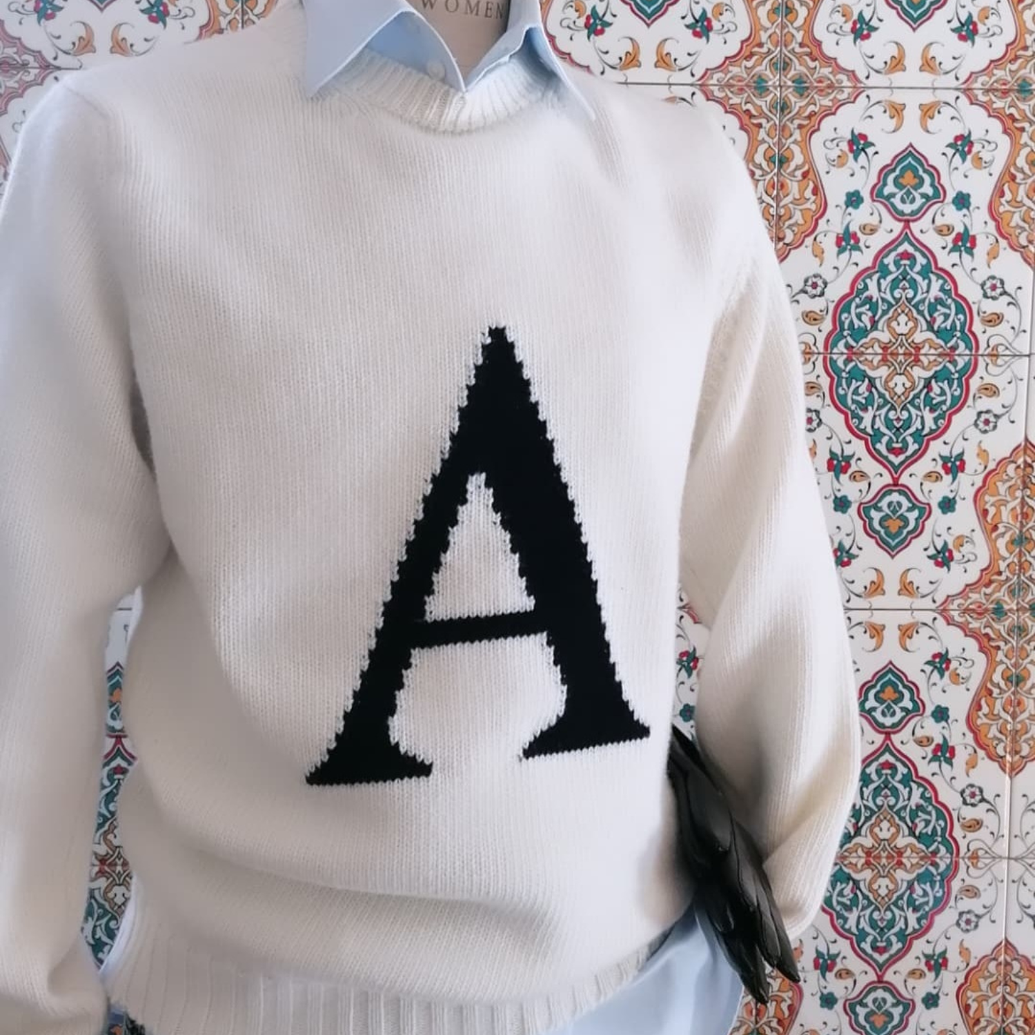 White sweater with a black letter 'A' on a patterned background