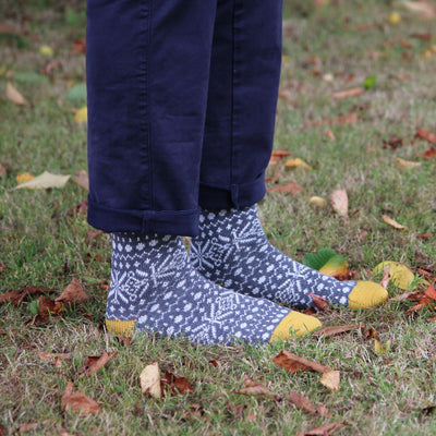Person wearing grey fair isle patterned socks with yellow accents standing on grass with fallen leaves.