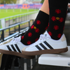 Person wearing black socks with red patterns and white Adidas sneakers on a stadium bench.