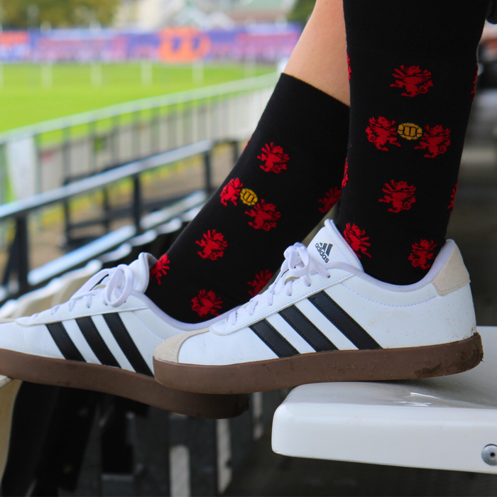 Person wearing black socks with red patterns and white Adidas sneakers on a stadium bench.