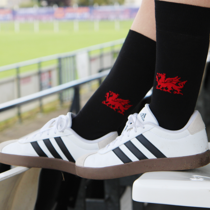 Person wearing black socks with red dragon designs and white sneakers with black stripes.