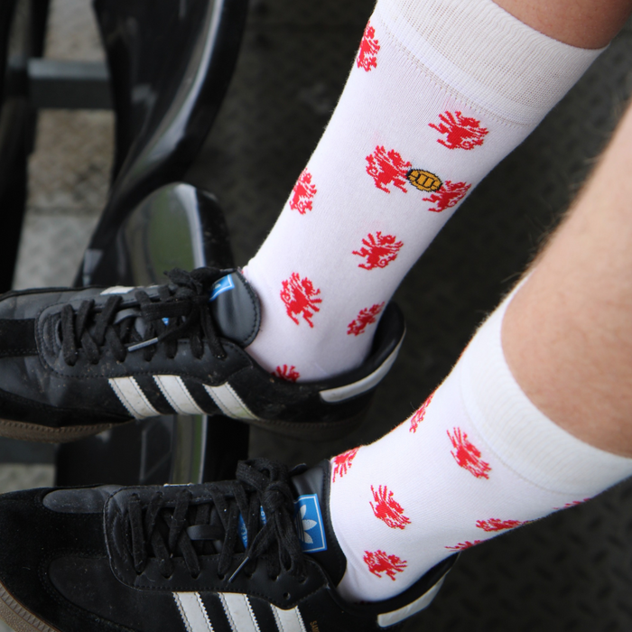 Person wearing white socks with red dragons and black trainers in a football stadium.