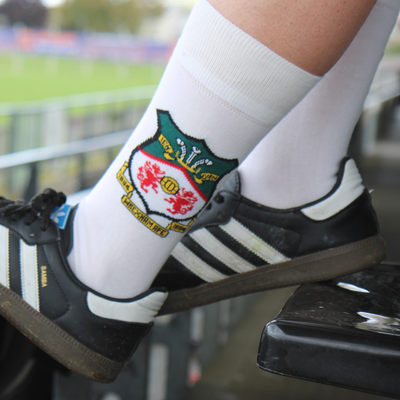 Person wearing white socks with a logo and black Adidas shoes in a stadium setting.