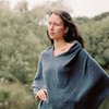 Woman wearing a charcoal poncho  standing outdoors with trees in the background
