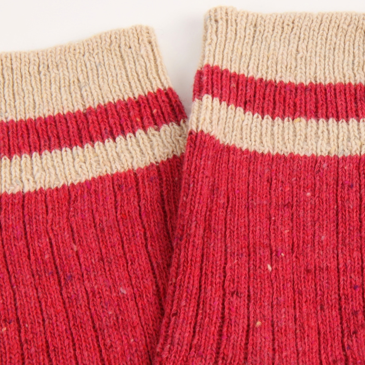 Close-up of a pair of pink knit socks with beige ribbed cuffs and a thin beige stripe near the top, shown against a plain light background.