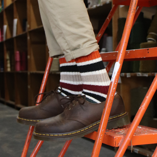 Person wearing brown shoes and striped socks on a ladder with yarn in the background