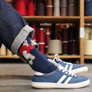 Person wearing navy blue socks with a red and white rugby player design, standing in front of spools of thread.