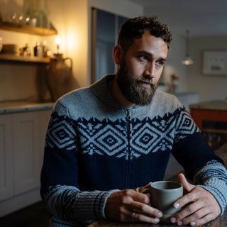 Man in a patterned sweater holding a mug in a kitchen.


