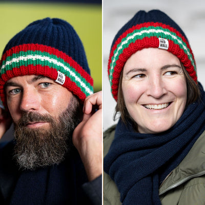 Two people wearing knit hats with red, green, and white stripes, one with a beard and the other smiling.