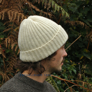 Person wearing a light cream knitted beanie in front of green foliage
