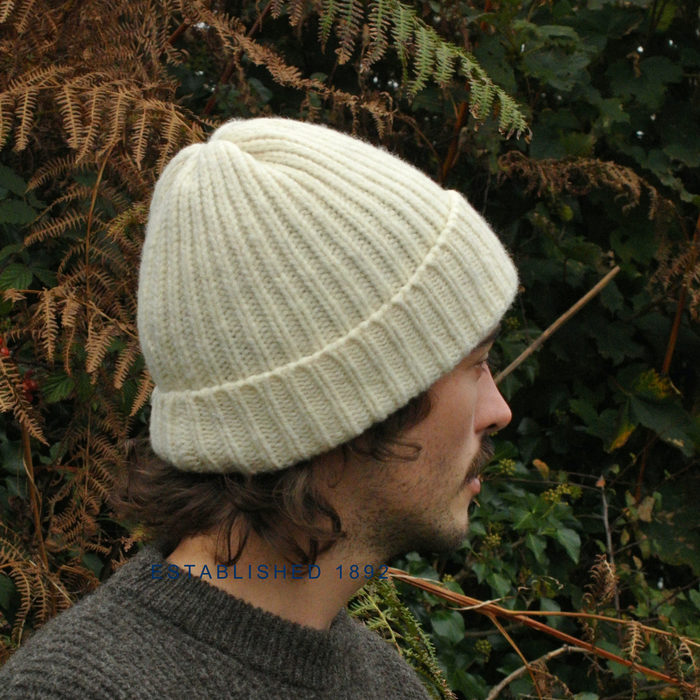 Person wearing a light cream knitted beanie in front of green foliage
