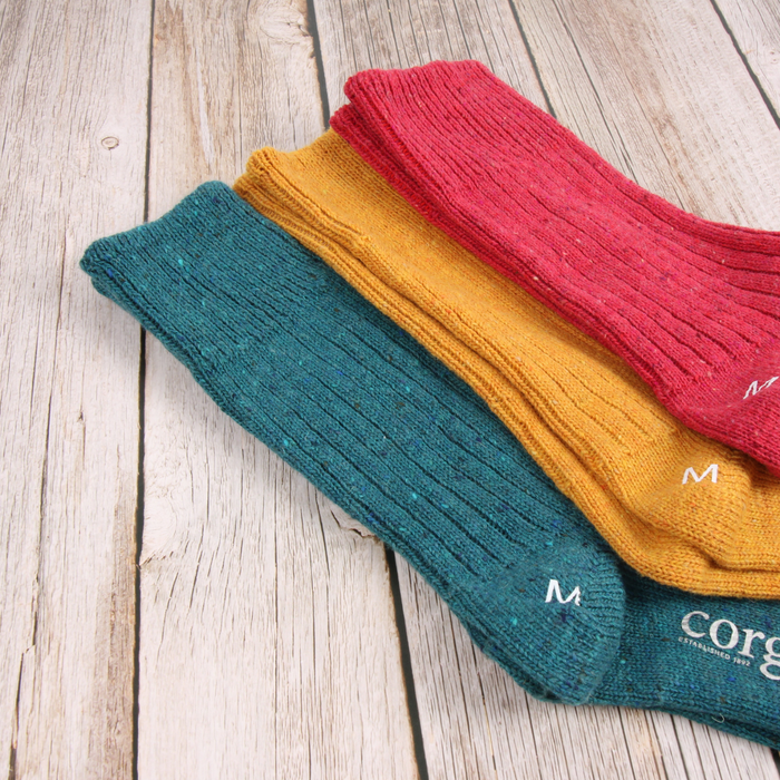 Three pairs of colorful socks stacked on a wooden surface, with 'Corgi' branding visible.