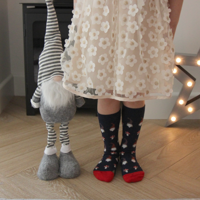 Person wearing a floral dress and patterned socks next to a gnome on a wooden floor.