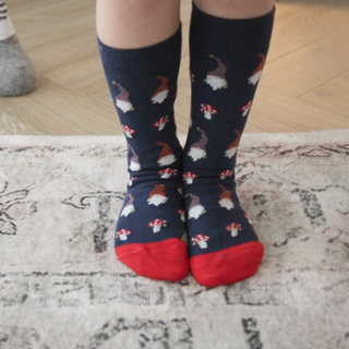 Navy socks with gnome and mushroom pattern worn by a person on a light wooden floor.