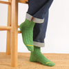 Green socks with a yellow accent worn by a person sitting on a wooden chair.