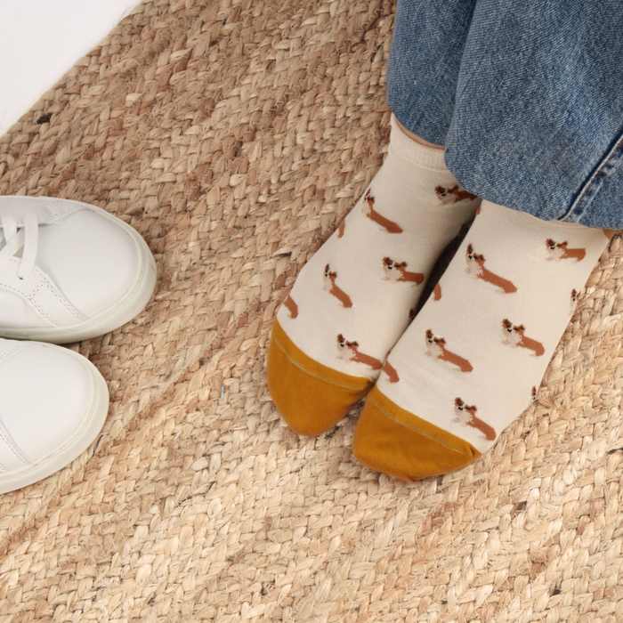 Person wearing socks with dog pattern and white sneakers on a woven surface