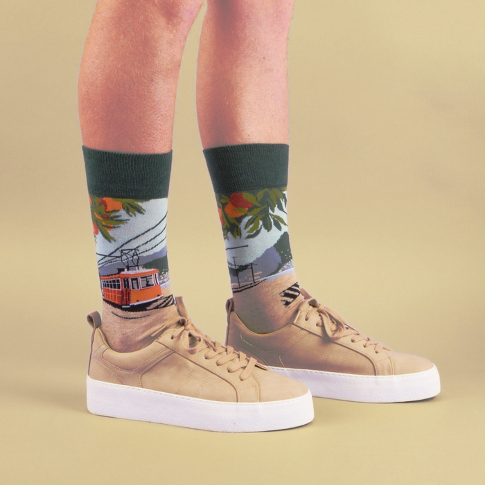 Person wearing socks with a tram design and tan sneakers on a beige background