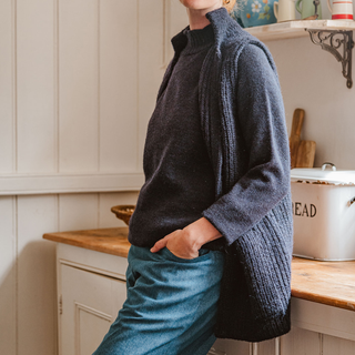Person wearing a dark blue sleeveless knitted gillet in a kitchen setting
